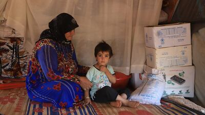 A mother and child in a camp for the internally displaced next to food aid provisions.