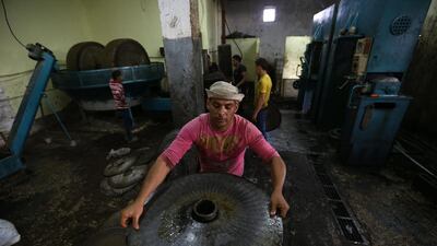 A worker prepares crushed olives between metal plates at a traditional stone press.