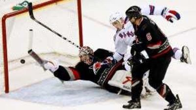 The Hurricanes' goalie Cam Ward tries to stop the puck as New York's Erik Christensen falls on him.