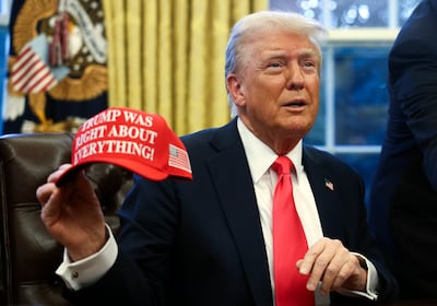President Donald Trump holds up a hat as he talks with reporters in the Oval Office at the White House in Washington. AP