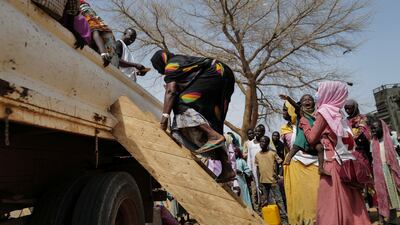 A Red Cross worker holds a child whose mother, a Sudanese who fled the conflict in Al Geneina in Darfur, climbs on to a lorry that will take them to a refugee camp in Chad. Reuters