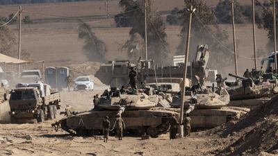Israeli soldiers organise equipment as they stand on tanks near the border with the Gaza Strip. Getty Images