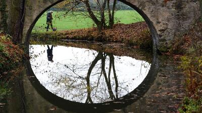 A woman reflects in the water of a creek as she walks past a small bridge at the Hanau-Wilhelmsbad state park in Hanau near Frankfurt am Main, western Germany. Arne Dedert / AFP