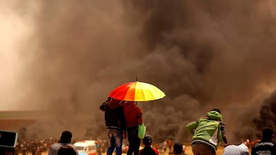 Two Palestinian boys hide from the sun as others burn tires at the border fence with Israel, east of Jabalia in the central Gaza city, during a protest. Mohammed Abed / AFP Photo