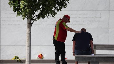 A security guard comforts a family member who lost a loved as he sits in front of the memorial wall where the names of the 185 killed are inscribed during the national memorial service. Getty Images