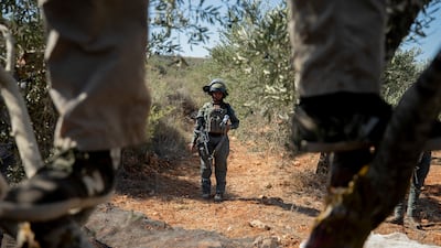 A man stands in an olive tree as an Israeli soldier observes nearby in the village of Baita, south of Nablus, in the occupied West Bank, last month. AFP