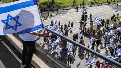 A demonstrator stands with an Israeli flag on an overpass above others march in Tel Aviv. AFP
