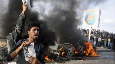 Opponents of Egyptian President Mohammed Morsi hold pamphlets urging a "no vote" on a constitutional referendum as cars burn during clashes between supporters and opponents of Mr Morsi in Alexandria, Egypt.