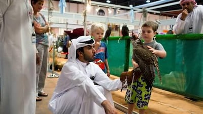 Kaelab Scott-Mackie, 4, pets a falcon as Ateeg Al Mazrooe, a captain in the Abu Dhabi Police, bottom left, looks to buy it at the Abu Dhabi International Hunting and Equestrian Exhibition.