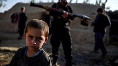 A young boy looks at the camera as a policeman holding a rocket-propelled grenade (RPG) stands behind in a house at Deh Qubad village in Maiwand district of Kandahar province, Afghanistan. AFP
