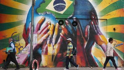 People pass graffiti of multi-coloured hands supporting the planet marked with a Brazilian flag on June 10, 2014 in Sao Paulo, Brazil. Mario Tama / Getty Images
