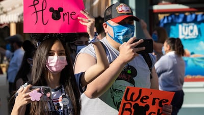 Returning guests wearing protective masks hold up signs on Main Street USA during the reopening of the Disneyland theme park in Anaheim, California, US, on Friday, April 30, 2021. Bloomberg