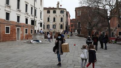 A Venetian wearing a protective mask walks by children playing in a square on in Venice, Italy. Getty Images