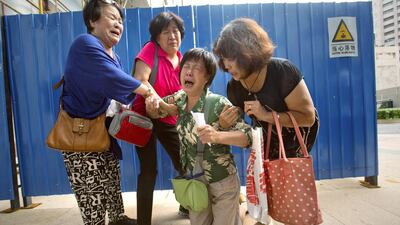Bao Lanfang, second from right, whose daughter-in-law, son, and granddaughter were aboard Malaysia Airlines Flight 370, kneels in grief while speaking to journalists outside the company's offices in Beijing on August 6. Mark Schiefelbein/AP