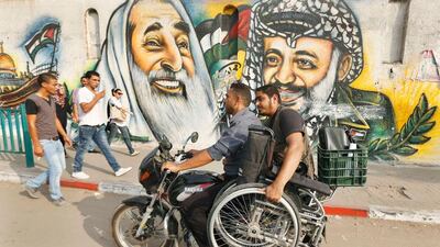 Moamen Qreiqea holds his wheelchair as he rides on a motorcycle past murals of late leader Yasser Arafat and late Hamas spiritual leader Ahmed Yassin, on a street in Gaza City.