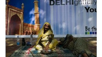 Homeless women sit in front of a Commonwealth Games sign. The government has been seeking to send migrants to their home states. Manpreet Romana / AFP