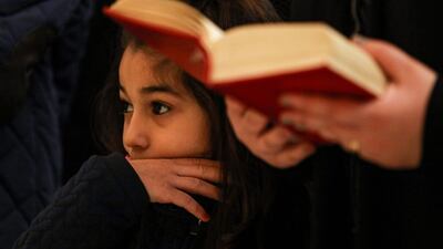 A girl looks on as a worshipper reads from a bible during the Christmas morning mass in Beirut. AFP