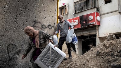 Displaced Palestinians carry personal belongings they retreived from their home as they walk past a bullet-riddled wall in the Jenin camp for refugees, in the occupied West Bank. AFP