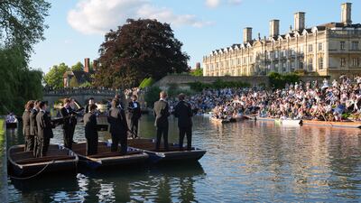 People sit on the banks of the Cam and lawns of King's College Cambridge to listen to The King's Men choir perform while standing in punts. PA
