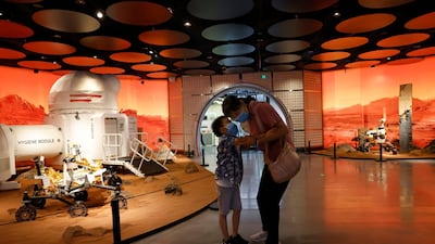 A child whispers to a woman as they visit an exhibition depicting rovers and bio-domes in Mars, in Beijing. AP Photo