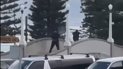 A screen grab from UGC video shows two gunmen dressed in black firing on a bridge at Bondi Beach in Sydney. Australian police said two people were taken into custody after reports of several gunshots. AFP