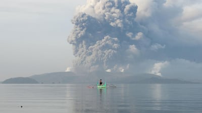 A youth living at the foot of Taal volcano rides an outrigger canoe while the volcano spews ash as seen from Tanauan town in Batangas. AFP