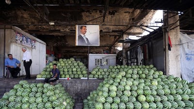 Syrian traders sit next to a portrait of Bashar Al Assad at a fruit and vegetable market in central Damascus. Joseph Eid / AFP Photo