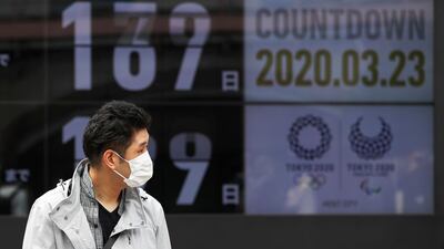 A passersby, wearing a face mask, walks past a screen counting down the days to the Tokyo 2020 Olympic Games in Tokyo. Reuters
