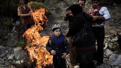 A family of refugees warm themselves by a fire upon arrival on the Greek island of Lesbos after crossing the Aegean sea from Turkey. Greece’s prime minister told the United Nations that Athens was doing all it could to help and criticised the building of walls to keep them out. Aris Messinis / AFP