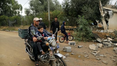 A Palestinian man and his son ride a motorcycle past the debris of a building destroyed in an Israeli air strike. Reuters