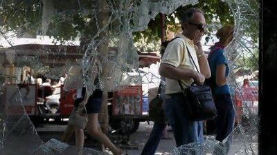 Athenians walk by a broken window of a building in central Athens on Thursday, June 30, 2011. Greek lawmakers are set to pass a bill Thursday to fast-track fresh austerity measures demanded by creditors following two days of rioting in Athens that left some 200 people injured. (AP Photo/Petros Giannakouris)