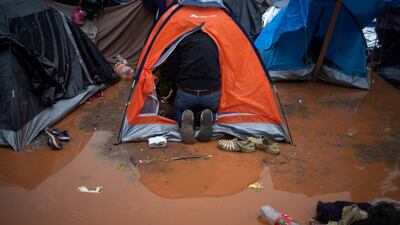 A migrant collects his belongings from his tent after rainfall. Reuters