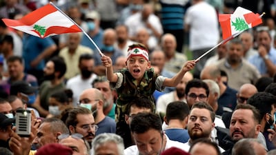 A boy wears military-style camouflage khakis and waves two Lebanese national flags at an anti-government protest. EPA