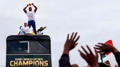 People cheer as South African Rugby captain Siya Kolisi (C) holds up the Web Ellis Trophy while the South African Rugby World Cup winner team parades on an open top bus through the streets of the city of Zwide , Port Elizabeth. AFP