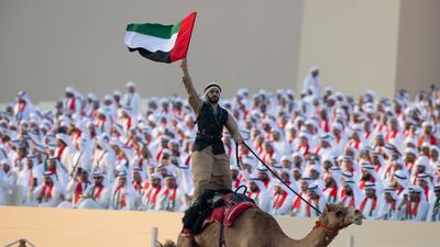 An Emirati man holding a UAE flag rides a camel during the Union Parade at the Sheikh Zayed Heritage Festival. Abdulla Al Neyadi / Presidential Court