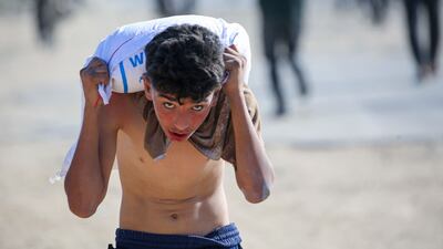 TOPSHOT - A displaced Palestinian youth ferries a bag of food aid on his shoulders after people stormed a World Food Programme warehouse in Deir el-Balah in the central Gaza Strip on May 28, 2025. The United Nations on May 28 condemned a US-backed aid system in Gaza following a chaotic food distribution where 47 people were injured, after Israel allowed supplies in at a trickle last week, easing a full blockade imposed on the besieged Palestinian territory for over two months. (Photo by Eyad BABA / AFP)