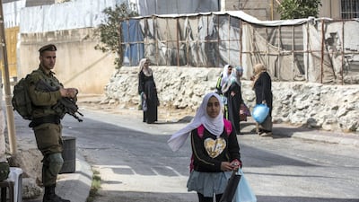 An Israeli soldier stands watch as Palestinian women and school children return home.