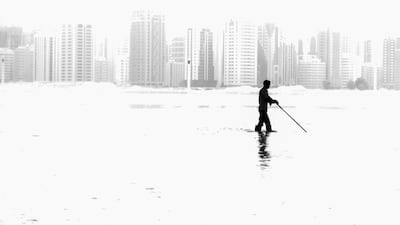 A member of the mantainence crew cleans the water feature in front of the Galleria at Sowwah Square while silloetted against the older skyline of Abu Dhabi’s Al Zahiyah area is seen in the heat haze from Al Maryah Island. Brian Kerrigan / The National