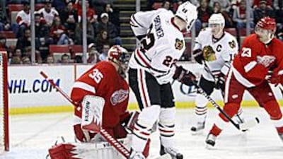 The Detroit Red Wings' goalie Jimmy Howard is tied up in goalmouth action with the Chicago Blackhawks' winger Troy Brouwer.
