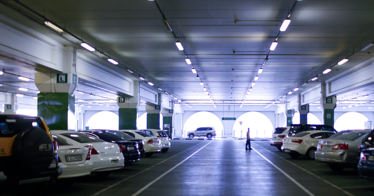 Spacious indoor parking garage in Dubai with multiple parked cars and a pedestrian walking through the lot|Arabwheels.ae