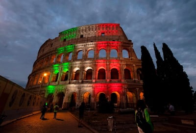 People walk in front of the Colosseum illuminated in the colours of the Italian flag. AFP