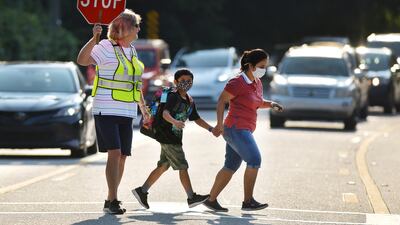 Crossing guard Kelly Linder helps a masked mother and son cross a road as they make their way to Loretto Elementary School on August 10, 2021, in Jacksonville, Florida, for the first day of the new school year. AP