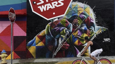 A man on a bicycle rides by a mural on a wall painted by graffiti artist Kobra in the Wynwood district during Art Basel in Miami, Florida, USA, 03 December 2015. Art galleries and artists from all over the world descend on Miami for the event which is considered one of the world’s largest art festivals with art events throughout the city. EPA