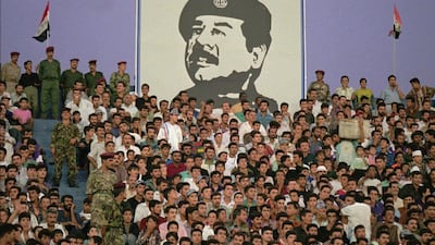 Football fans sit under a portrait of Saddam Hussein at Al Sha'ab Stadium in Baghdad in 1996. Faisal Al Yafai imagines a world where Saddam maintained control over Kuwait. (John Moore / AP Photo)