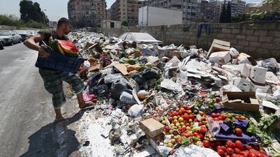 A Lebanese man throws more trash on a pile of rubbish covered with white pesticide in the Palestinian refugee camp of Sabra in Beirut on July 23. Bilal Hussein/AP