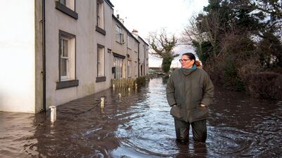 Gabrielle Burns-Smith stands outside her flooded home on the outskirts of Lymm in north west England. Almost the whole of England, Wales and Northern Ireland are subject to weather warnings for rain until Thursday morning. AP Photo