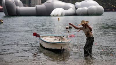 A fisherman sorts his net next to the 37-meter-long 'KAWS:HOLIDAY' 'Companion' inflatable sculpture in Tsing Yi, Hong Kong. EPA