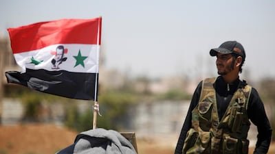 A soldier stands in the Deraa countryside next to a Syrian flag with an image of Bashar Al Assad on it. Reuters