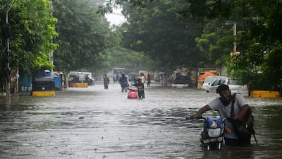 Commuters push their motorcycles through deep water after the floods inundated Chennai's streets. AFP