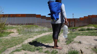 A migrant carrying a toddler stands in front of the border wall that divides Sunland Park, New Mexico, with the Mexican state of Chihuahua. AFP